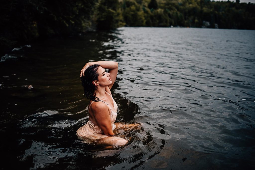 Woman sitting on a rock in the lake during her outdoor boudoir photoshoot