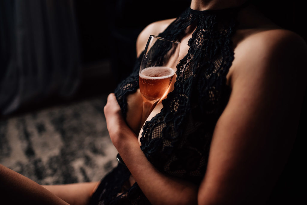 client poses with glass of champagne for creative boudoir photographer